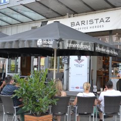 Menschen sitzen vor dem Cafe "Baristaz" und hören der Leserin zu.